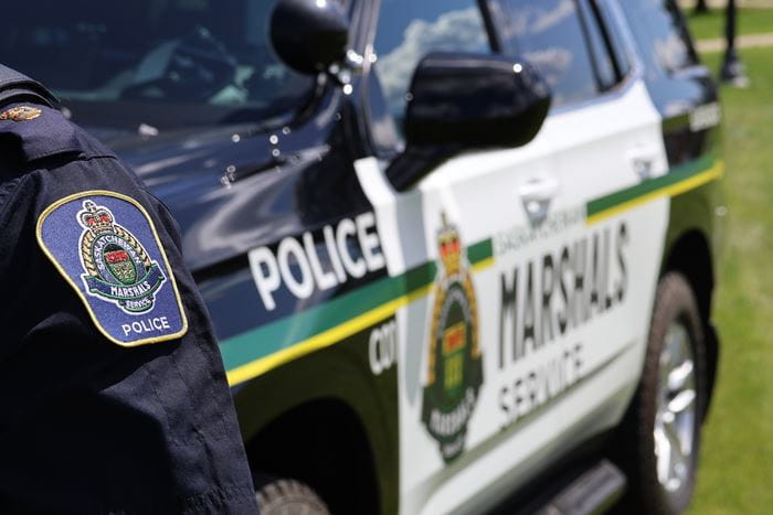 A Saskatchewan Marshal stands Infront of a police cruiser. 